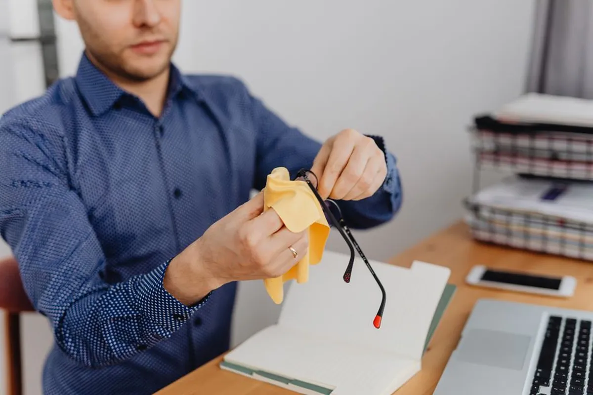 Homme essuyant ses lunettes avec un chiffon, assis à un bureau